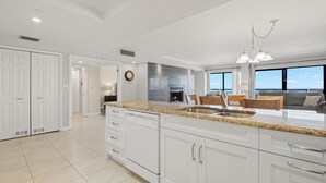 A spacious kitchen with white cabinets, a granite countertop, and a large window overlooking the sea.