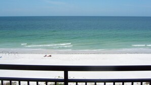 A beach with a railing in the foreground, a clear sky, and calm sea.