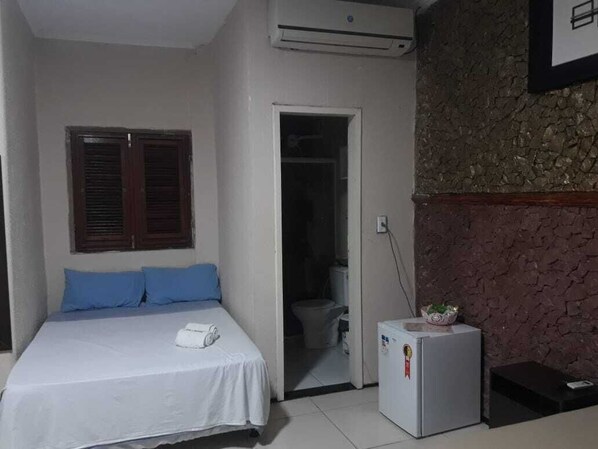 A bedroom with a bed, a small refrigerator, and a bathroom visible through an open door. - Hotel Nacional (Sobral)