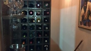 Una bodega con varias botellas, un cubo, un electrodoméstico blanco y un cuadro en la pared.