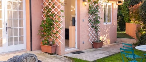 A house with a garden, a patio with chairs, and a door with a window.