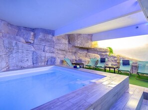A swimming pool with a stone wall, lounge chairs, and a small table.