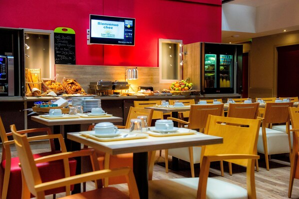 A restaurant with tables set for dining, a buffet with bread and fruits, and a TV screen displaying a welcome message.