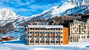 Ett hotell med flera våningar, en skidbacke i bakgrunden och snötäckta berg.