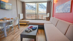 Ett modernt hotellrum med en stor säng, en soffa, ett matbord med stolar, ett litet soffbord och utsikt över ett snötäckt berg genom stora fönster.