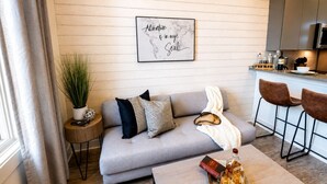 A modern living room with a grey sofa, a coffee table, and a bar area with stools. A framed inspirational quote is on the wall. - Comfortable condo near Vanderbilt with easy access to local attractions (Nashville)