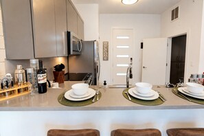 Een moderne keuken met een centraal eiland, roestvrijstalen apparatuur en een 'WELCOME' bord.