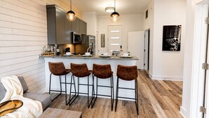 A modern kitchen with a bar area, wooden flooring, and a sofa with a throw blanket.