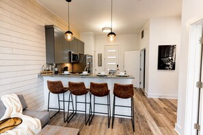 A modern kitchen with a bar area, wooden flooring, and a sofa with a throw blanket. - Comfortable condo near Vanderbilt with easy access to local attractions (Nashville)