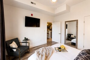 A hotel room with a bed, a chair, a small table with a plant, a TV mounted on the wall, and a mirror reflecting the room. - Comfortable condo near Vanderbilt with easy access to local attractions (Nashville)