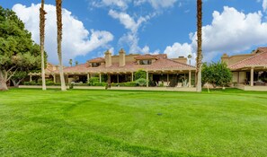 A large, multi-story residential building with a red-tiled roof, surrounded by well-maintained lawns and tall palm trees. - WOW! Gorgeous Desert Condo Woodhaven Country Club (Palm Desert)