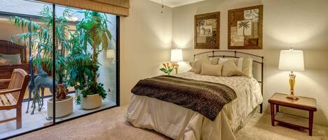 A bedroom with a bed, two bedside tables with lamps, a ceiling fan, and a large window with a view of a patio area.