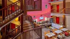 Hotelinnenraum mit mehreren Ebenen, einer zentralen Treppe, einem Speisebereich und einem Fernsehbildschirm.