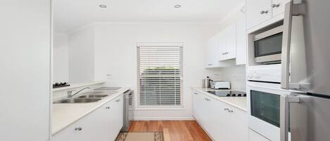 A narrow kitchen with white cabinets, a built-in oven, a microwave, and a sink.