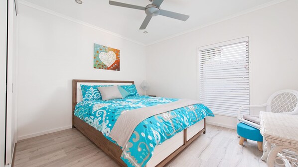 A bedroom with a bed, a ceiling fan, a window with blinds, and a small chair.