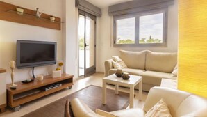 Una sala de estar moderna con una televisión de pantalla plana, un sofá, una mesa de centro y un ventanal corredizo que da a un balcón.