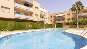 Una piscina rodeada de edificios de apartamentos con balcones, cielo despejado y una palmera.