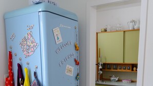 Ein Zimmer mit einem blauen Kühlschrank, einem roten Stuhl und einer Küchenzeile mit grünen Schränken und einer weißen Arbeitsplatte.