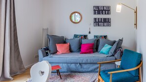 Ein modernes Wohnzimmer mit einem grauen Sofa, bunten Kissen, einem blauen Sessel, einem weißen Stuhl und einem gemusterten Teppich.