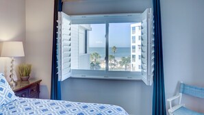 Un dormitorio con cama, una mesita de noche con lámpara, una planta en maceta y una ventana con cortinas.