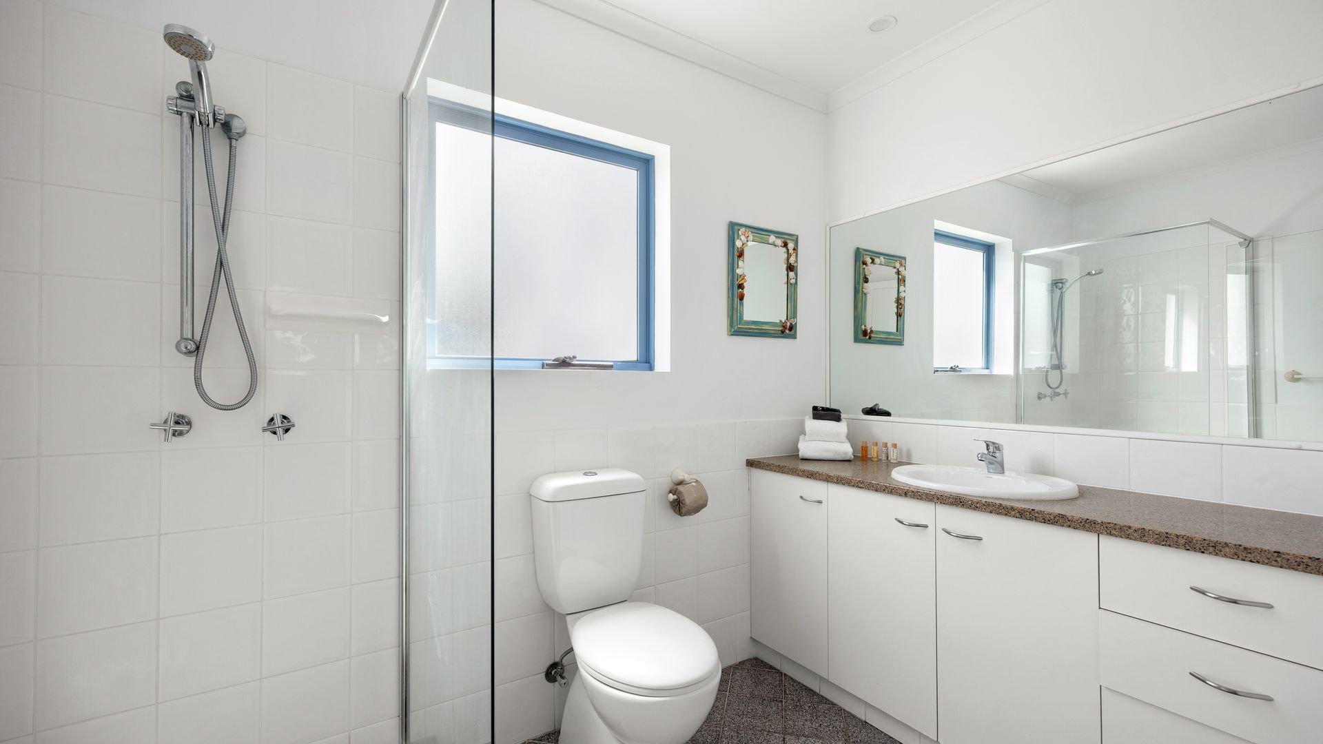 A modern bathroom with a glass shower enclosure, a white toilet, a sink with a granite countertop, and a large mirror.