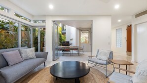 Ein modernes Wohnzimmer mit Sofa, Sessel, Couchtisch und einer Essecke mit Grill.