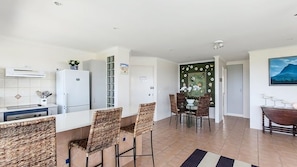 A modern kitchen with white cabinets, a built-in oven, and a refrigerator. There is a dining area with a table and chairs, and a decorative wall with a floral pattern.