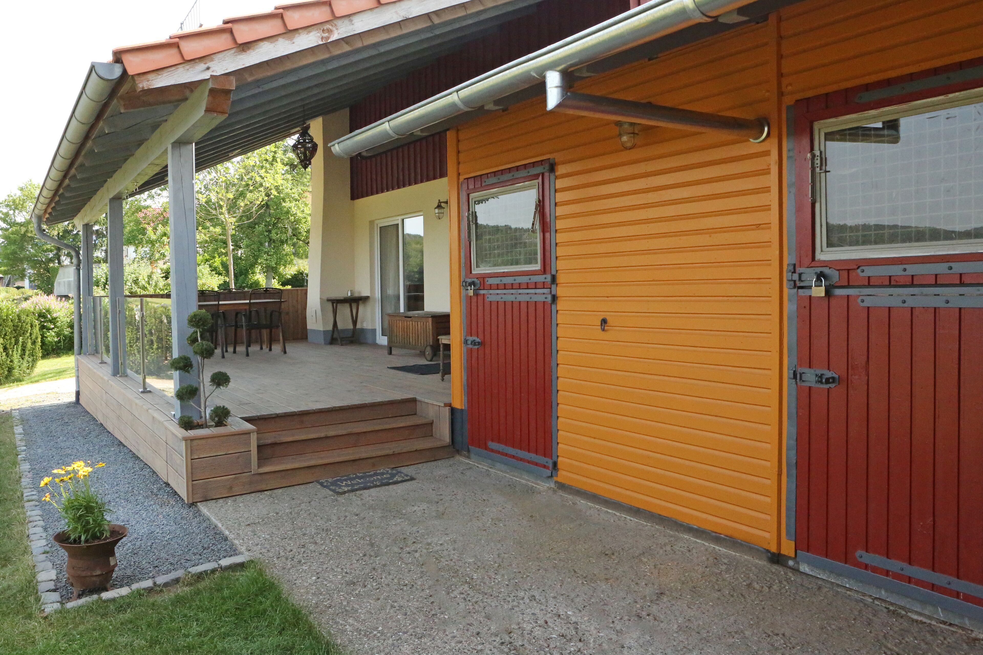 A two-story building with a covered porch, a red door, and a yellow exterior wall.