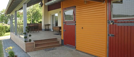 A two-story building with a covered porch, a red door, and a yellow exterior wall.
