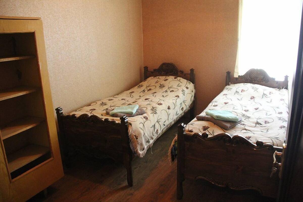 A bedroom with two wooden beds, a wooden wardrobe, and a window.