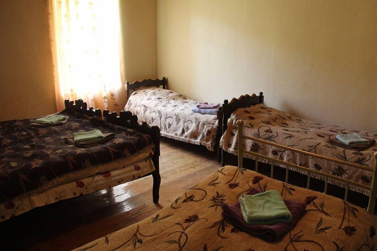 A room with two single beds, a wooden floor, and a window with curtains.