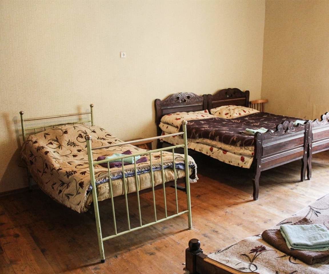 Two single beds with metal frames, a wooden floor, and a small table with a book and a bottle.