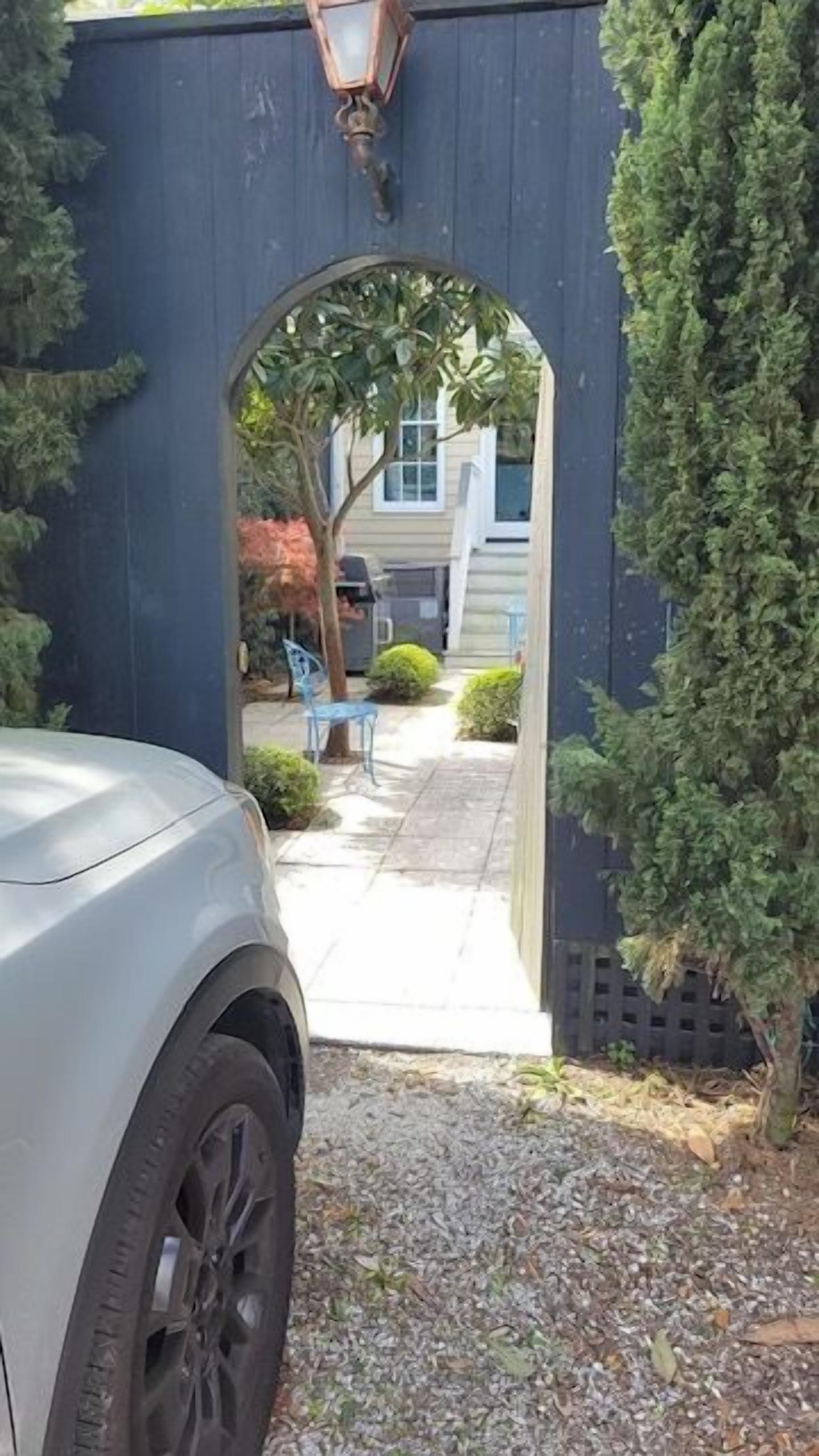 A driveway leading to a house with a covered carport and a small garden area.