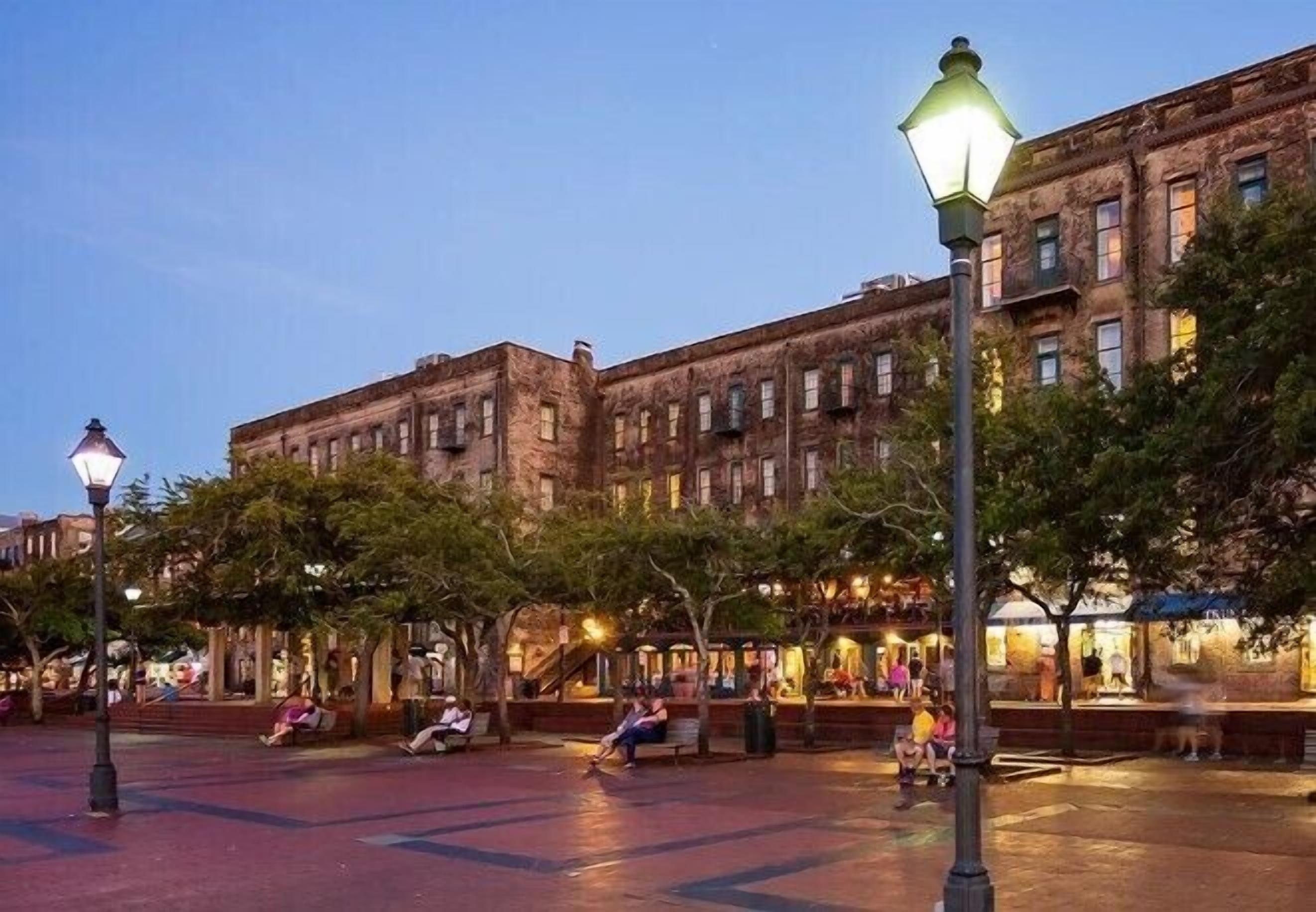 A public square with benches and trees, surrounded by historic buildings with multiple stories and windows.