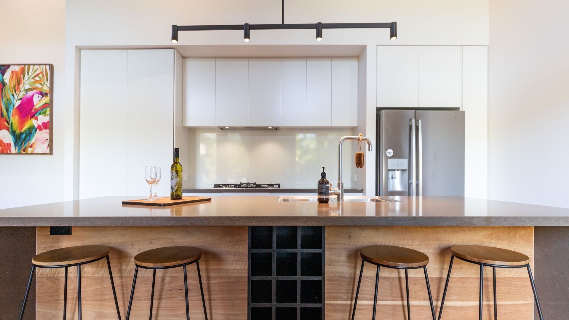 A modern kitchen with a large island, bar stools, a refrigerator, and a colorful painting on the wall.