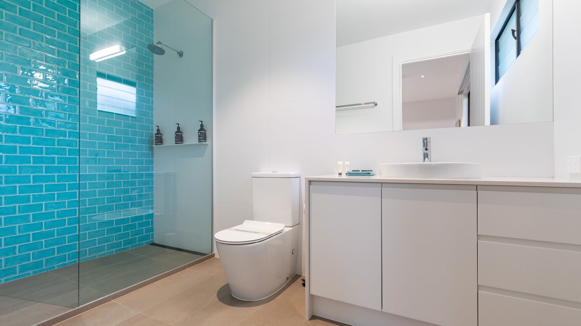 A modern bathroom with a glass shower enclosure, a white toilet, and a sink with a mirror above it.