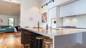Una cocina moderna con una isla grande, taburetes de bar, un reloj y un cuadro abstracto y colorido.