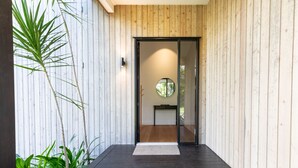 Una entrada moderna con fachada de madera, puerta de vidrio y un pequeño espacio interior con un espejo circular y un banco.