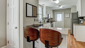 A modern kitchen with white cabinets, a granite countertop, and two wooden bar stools.