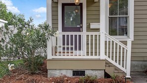 A house with a front porch, a dark front door, a white railing, and a window with blinds.