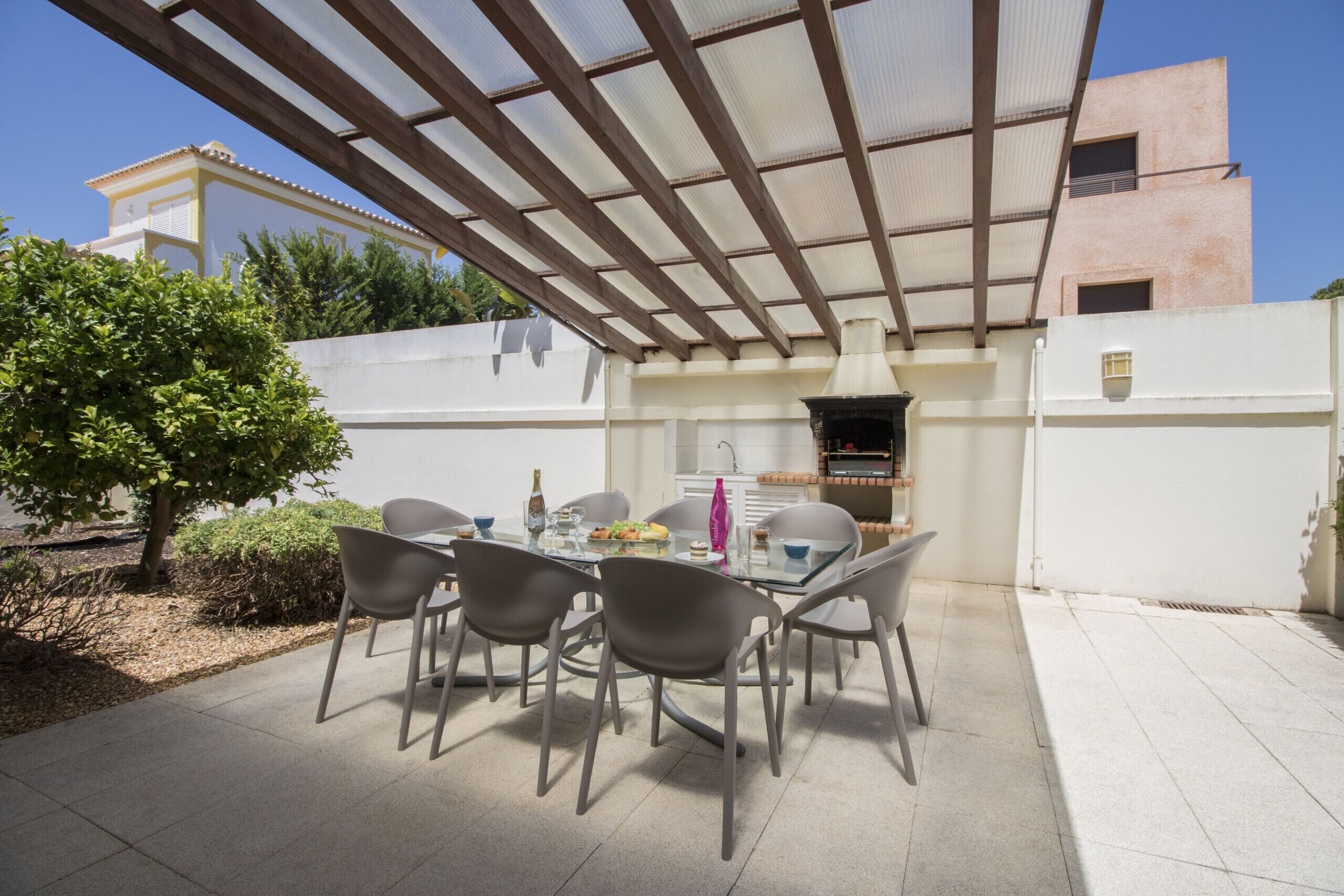 Eine Terrasse im Freien mit Tisch, Stühlen, einem Grill und einer Pergola.
