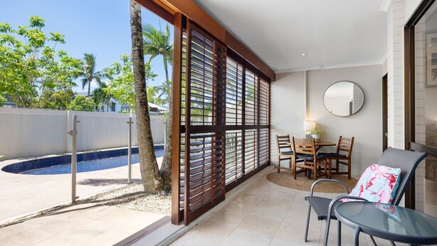 Eine moderne Außenpatio mit Pool, Holz-Privatsphärenwänden, einer Essecke mit Stühlen und Tisch sowie einem Glastisch mit einem Stuhl.