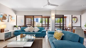 Ein modernes Wohnzimmer mit zwei blauen Sofas, einem Glastisch und einem Deckenventilator.