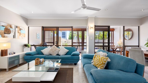 A modern living room with two blue sofas, a glass coffee table, and a ceiling fan. - Ballater 2 Noosa Heads (Noosa Heads)
