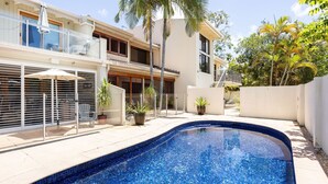 Ein modernes Haus mit Swimmingpool, Sitzgelegenheiten im Freien und tropischen Pflanzen.
