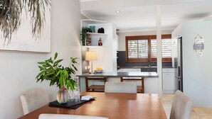 Eine moderne Küche mit einer zentralen Kochinsel, ein Essbereich mit Holztisch und Stühlen sowie eine Wohnbereich mit Sofa und Couchtisch.
