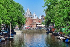 Un edificio histórico con múltiples agujas, un canal con barcos y frondosos árboles verdes.