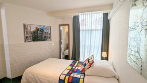 Una habitación de hotel con una cama, un cuadro, una ventana con cortinas y una lámpara.