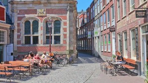 Una calle adoquinada con mesas al aire libre y un edificio histórico de fachada roja y ventanas arqueadas.