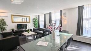 Una sala de estar moderna con una mesa de comedor de vidrio, sofás negros, un televisor de pantalla plana y un espejo grande.